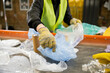 © LIGHTFIELD STUDIOS - Cropped view of blurred worker in protective vest and gloves taking plastic bag from conveyor while working in waste disposal station at background, garbage sorting concept