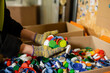 © LIGHTFIELD STUDIOS - Cropped view of female sorter in protective gloves holding colorful plastic caps near carton boxes while working in waste disposal station, garbage sorting and recycling concept
