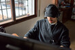 Young man working on the computer. He wears a cap that covers half of his face.