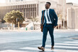 © Sivu G/peopleimages.com - Happy businessman, walking and city to work for travel on street or pedestrian crossing outdoors. Black man on cross road, walk or traveling to business with suit and smile on asphalt in urban town