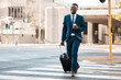 © Sivu G/peopleimages.com - Travel, business and black man with suitcase in city for international conference, global trip and meeting. Corporate, happy and male entrepreneur with luggage for journey, commute and convention
