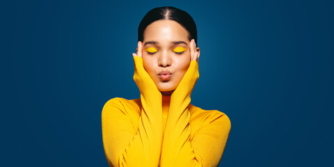 Radiating self-love: Young woman with colourful makeup embraces her face in a studio