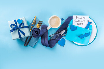 Wall Mural - Accessory and decor arranged Father's Day greeting card, Dad`s holiday flat lay, table setting with envelope, postcard, mustaches, napkin, tie, coffee and gift box on blue background