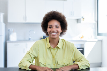 Joyful happy short haired Black business woman sitting at workplace in home office, looking at camera, smiling. Millennial worker, employee, entrepreneur head shot portrait.