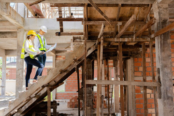 Wall Mural - Two Asian male and female engineers looking at blueprints and listnotes. walking on stairs in the design of construction work about architecture For future industries, wear vests and helmets.