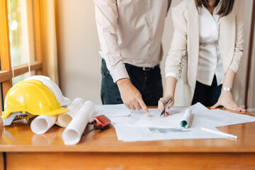 Wall Mural - Half-body shot of 2 male and female architects, similar to engineers, pointing at a blueprint on a desk with a pen. About construction industry projects in the office, helmets and walkie-talkies.