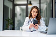 © bnenin - A serious female doctor using a mobile phone while sitting at the office table.