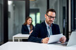 © bnenin - A serious businessman reading documents while working over a laptop at the office.