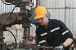 © amorn - Male factory worker working at work maintenance machine in industrial factory while wearing safety uniform, glasses and hard hat. Male technician and heavy steel lathe machine in workshop