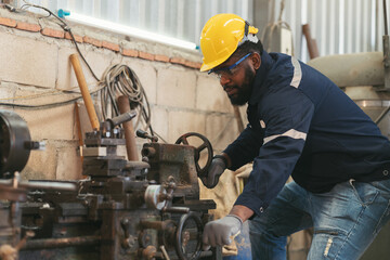 Wall Mural - Male factory worker working at work maintenance machine in industrial factory while wearing safety uniform, glasses and hard hat. Black male technician and heavy steel lathe machine in workshop