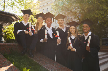 Wall Mural - Happy college graduates standing in row with diplomas. Smiling graduate students in black mortar board caps and bachelor gowns celebrating college or university graduation