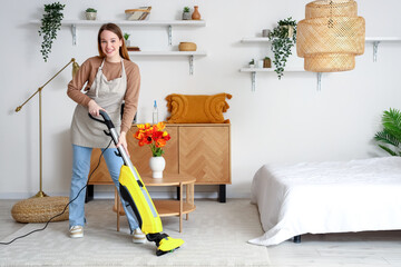 Wall Mural - Young woman hoovering carpet in bedroom