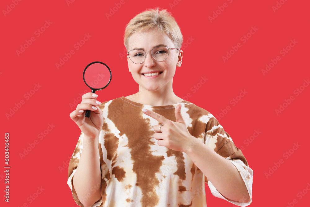 Young woman pointing at magnifier on red background