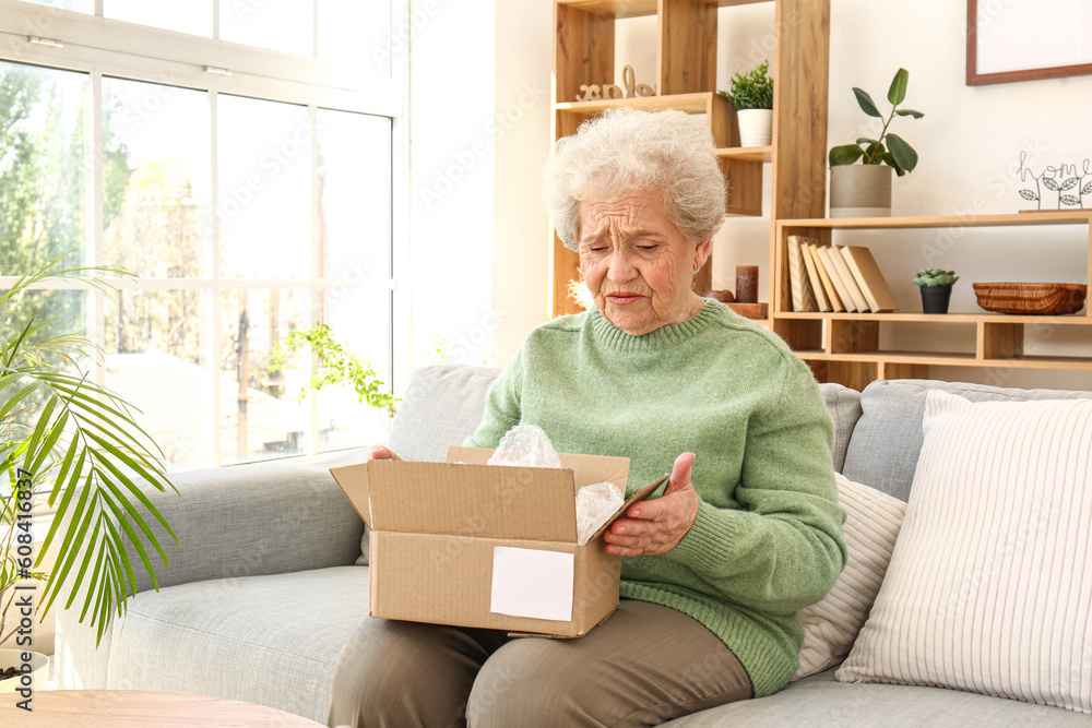 Upset senior woman opening parcel at home