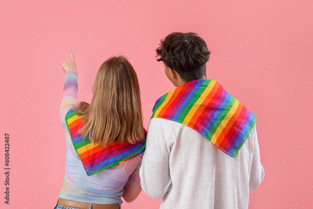 Young couple with LGBT flags pointing at something on pink background, back view
