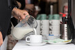 Frau füllt am Buffet Milch aus einer Karaffe in eine Kaffeetasse
