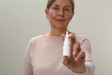 Poster - Woman holding nasal spray on light grey background, focus on bottle