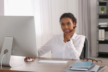 Canvas Print - Smiling African American intern working with computer at table in office