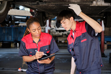 Two professional automotive worker partners discuss mechanical check undercarriage of lifted electric car, fix and repair at maintenance garage, and expert service business works industry occupation.