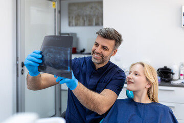 Wall Mural - Doctor talking with her patient and teaching a radiograph. Dentist concept of woman sitting in a dental chair while her dentist reads out an x-ray scan