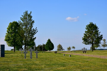 Wall Mural - A view of an old historic cemetery located in the middle of a well maintained field or meadow, with stone and wooden crosses, marble blocks, and some benches seen next to a well maintained path