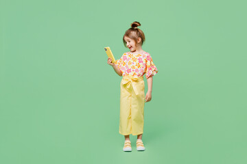 Wall Mural - Full body fun little child kid girl 6-7 years old wear casual clothes hold in hand use mobile cell phone isolated on plain pastel green background studio. Mother's Day love family lifestyle concept.