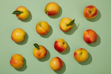 Wall Mural - Top down flat lay colorful shot with fresh ripe peaches (prunus persica) on pastel green background. Minimal scene for advertising product with peach ingredient.