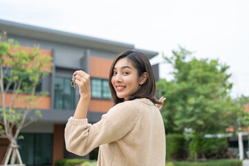 Woman buying or rent new home she holding key front of new house. Surprise happy young asian woman giving house key and smile to rent or purchase apartment home. Moving relocation concept.