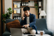 © Nuttapong punna - Young business man working at home office with laptop, tablet and taking notes on the paper. meeting video conference doing market research working on sofa