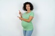 © Roquillo - Beautiful pregnant woman wearing green T-shirt standing over white studio background points at copy space indicates for advertising gives right direction