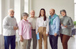 Group portrait of happy old people and young business coach. Elderly men and women with pencils and notebooks standing together with coach girl, looking at camera and smiling. Senior education concept