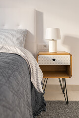 Close-up of a bedroom with a double bed and a wooden bedside table in light colors and a lamp. The concept of a stylish comfortable bedroom for a young family