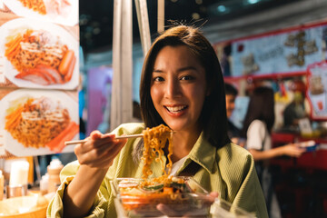 Wall Mural - Asian woman enjoy eating noodles street food at night market. Traveler Asian blogger women Happy tourists Beautiful female with Traditional thailand bangkok food.