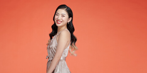 Wall Mural - Attractive asian young woman standing on red background, wearing silver evening dress