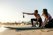 A Surf Instructor Is Pointing At Good Wave While A Girl Smiling And Watching.
