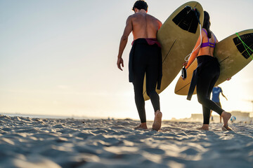 Wall Mural - Rear view of couple of surfers carry surfboards on the beach.