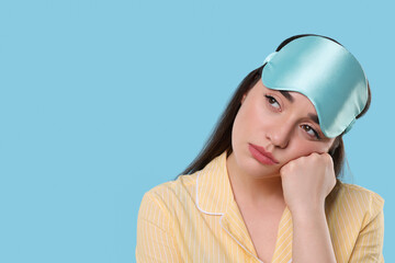 Canvas Print - Tired young woman with sleep mask on light blue background, space for text. Insomnia problem