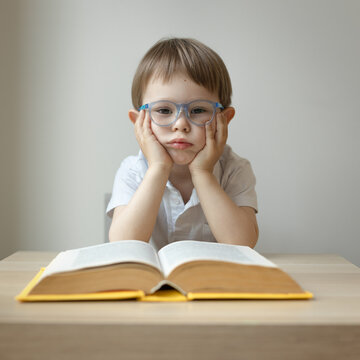 Wall Mural - boy 3 years old sits at a desk and is bored in front of an open book, dyslexia concept, boring school