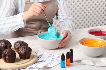 Wall Mural - Woman mixing cream with light blue food coloring at white wooden table, closeup. Decorate cupcakes