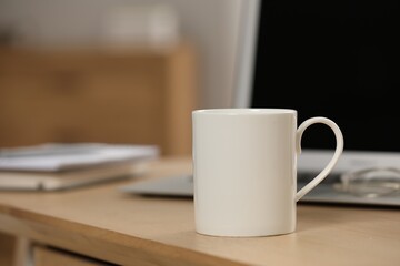 Wall Mural - White ceramic mug and laptop on wooden table at workplace. Space for text