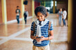 © Drazen - Happy black teenage girl using mobile phone in high school hallway.