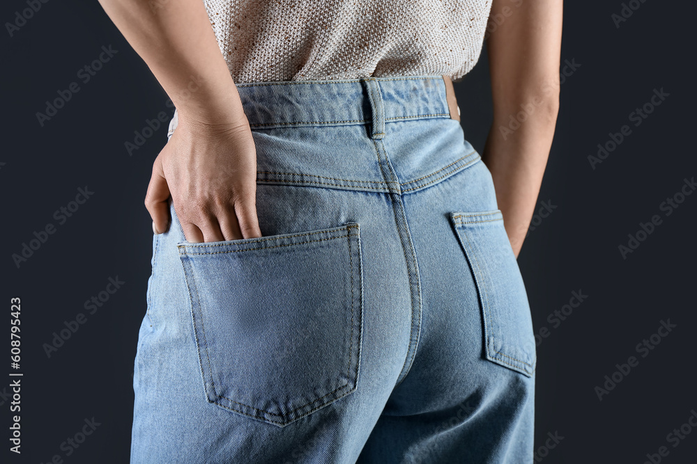 Young woman in stylish jeans on dark background, back view