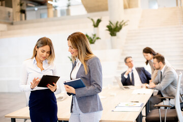 Wall Mural - Two young business women looking at financial results on digital tablet in front of their team at the office