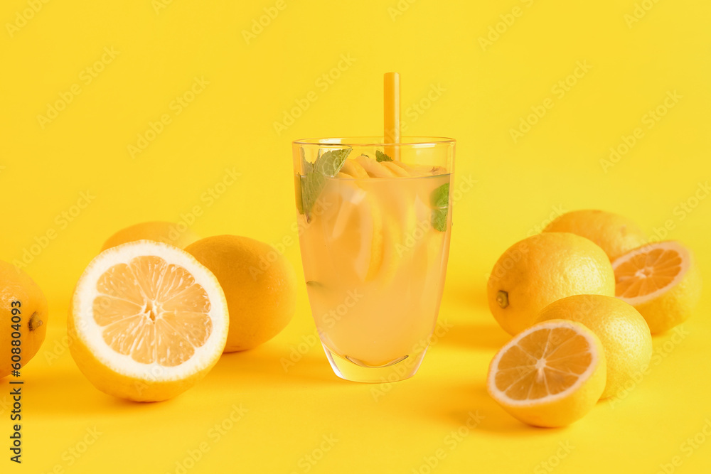 Glass with fresh lemonade and lemons on yellow background