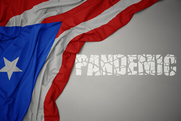 waving colorful national flag of puerto rico on a gray background with broken text pandemic. concept.