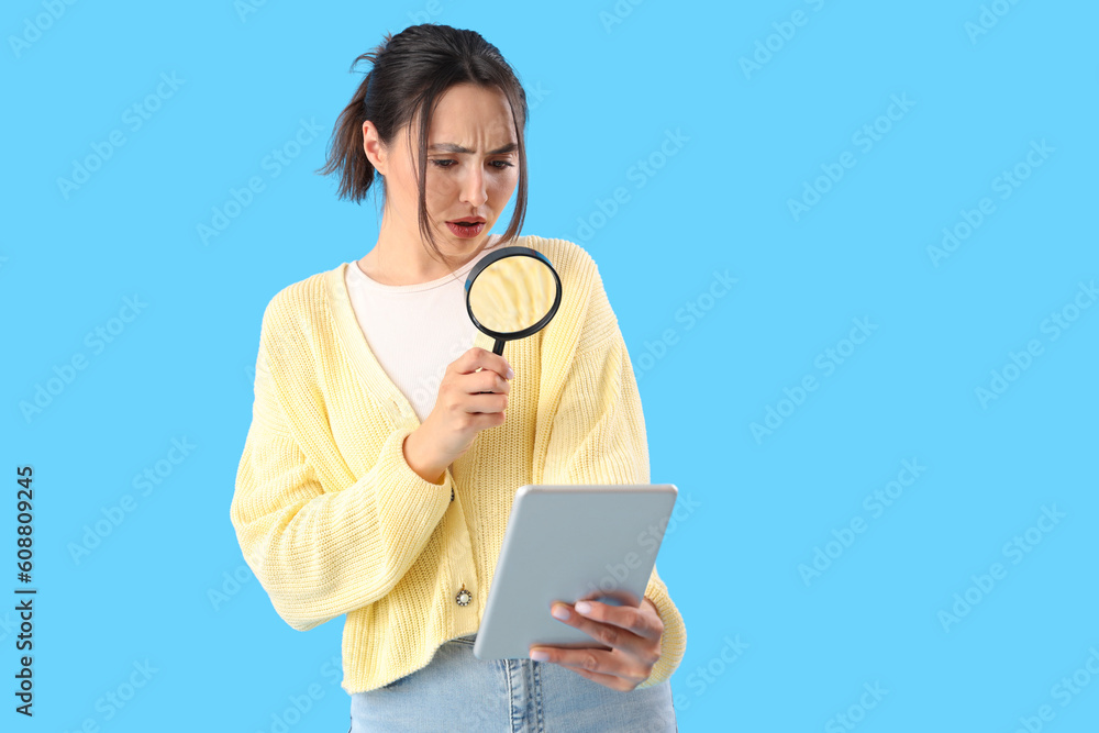 Young woman with magnifier and tablet computer on blue background