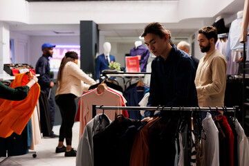 Diverse people shopping in clothes shop, look for red-hot Black Friday deals. Customers looking through clothing items on hangers in fashion boutique, exploring new fashion collection at outlet store