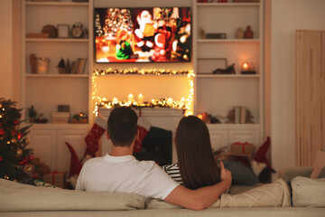 Wall Mural - Couple watching Christmas movie via TV in cosy room, back view. Winter holidays atmosphere