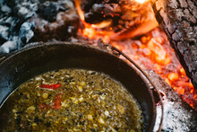 A rustic soup in a cast iron pot over red hot coals