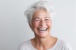 Close up portrait of a happy senior woman laughing while standing against grey background